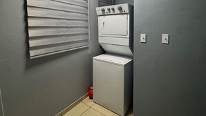 A laundry room with a stacked washer and dryer, a window with blinds, and a tiled floor. - Modern Townhouse Near Beaches & BQN Airport with Pool (Aguadilla)
