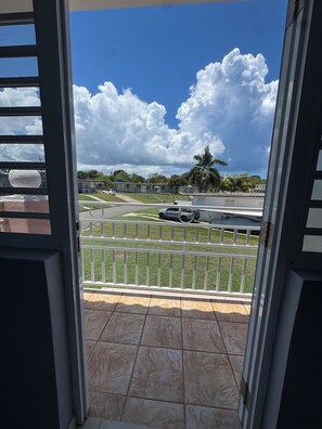 Un balcon donnant sur une rue, une voiture garée et un bâtiment en arrière-plan.
