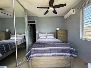 Une chambre à coucher comprenant un lit, une armoire, un ventilateur de plafond, un appareil de climatisation et une fenêtre avec des stores.