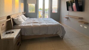 A bedroom with a bed, a nightstand, a ceiling fan, a TV, and a window with blinds. - Modern Townhouse Near Beaches & BQN Airport with Pool (Aguadilla)