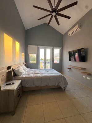 A bedroom with a bed, a nightstand, a ceiling fan, a TV, and a window with blinds. - Modern Townhouse Near Beaches & BQN Airport with Pool (Aguadilla)