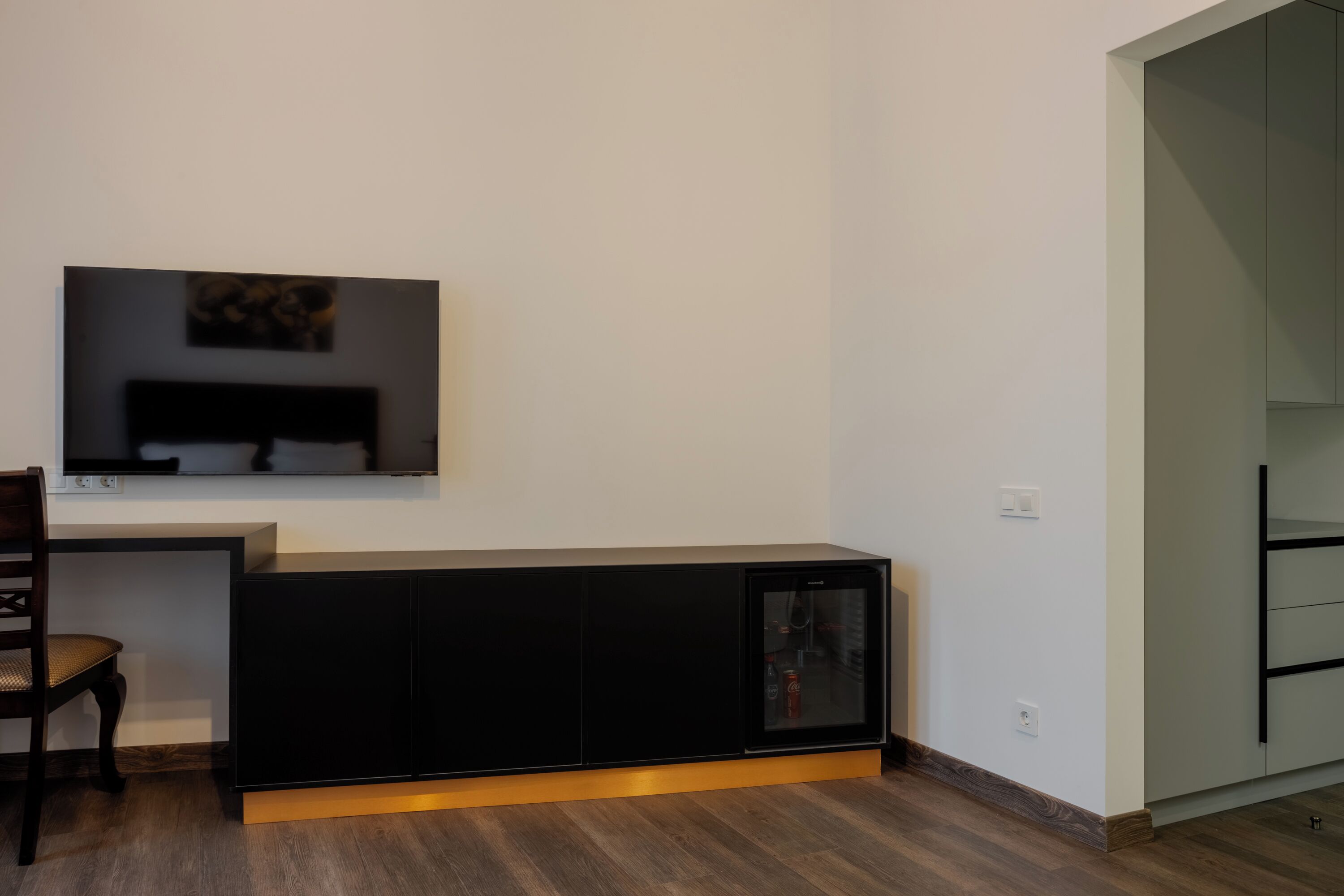 Un salon moderne avec un meuble de rangement noir pour les appareils électroniques, un téléviseur à écran plat fixé au mur et un plancher en bois.