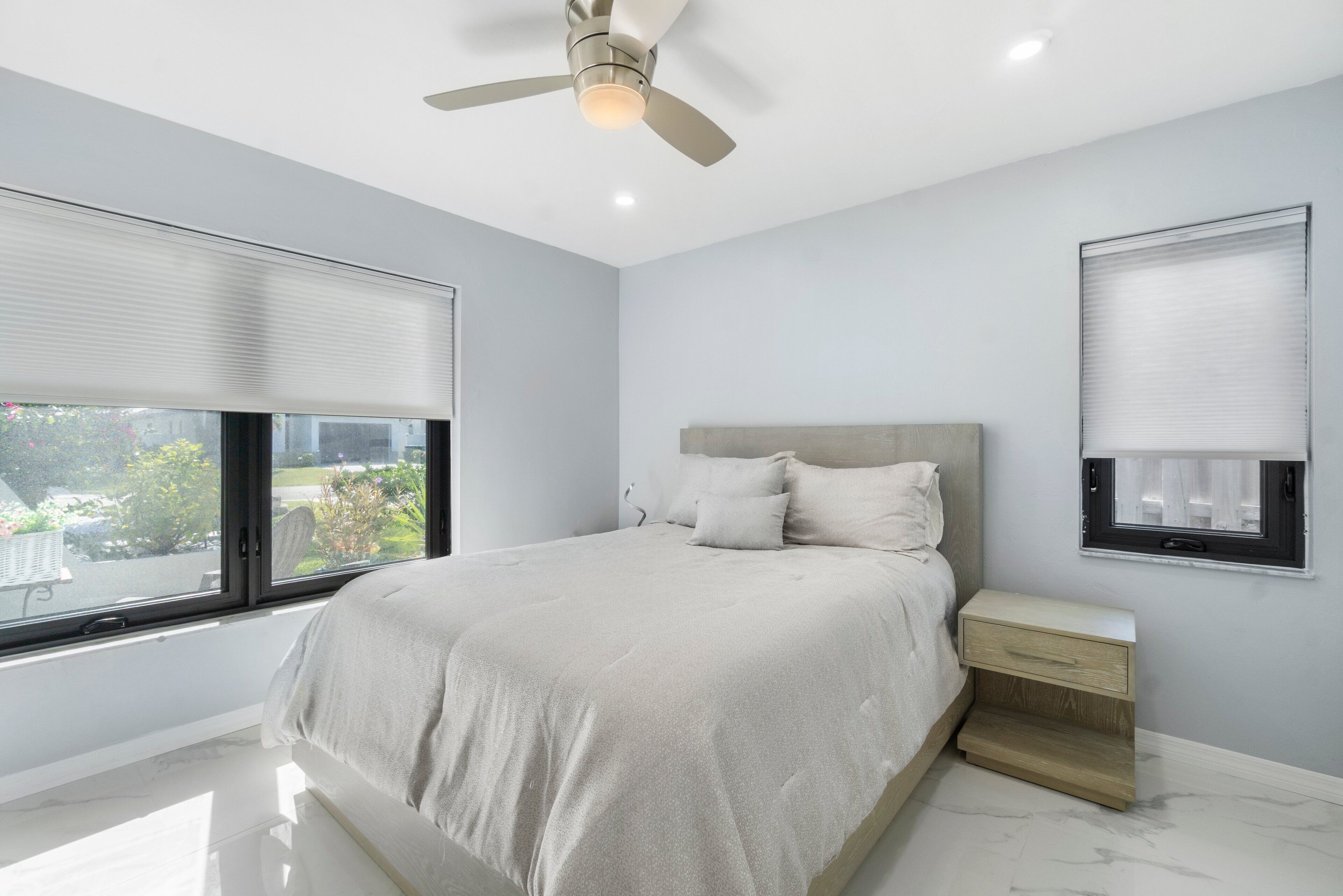 Quarto com cama, mesa de cabeceira e ventoinha no teto.
