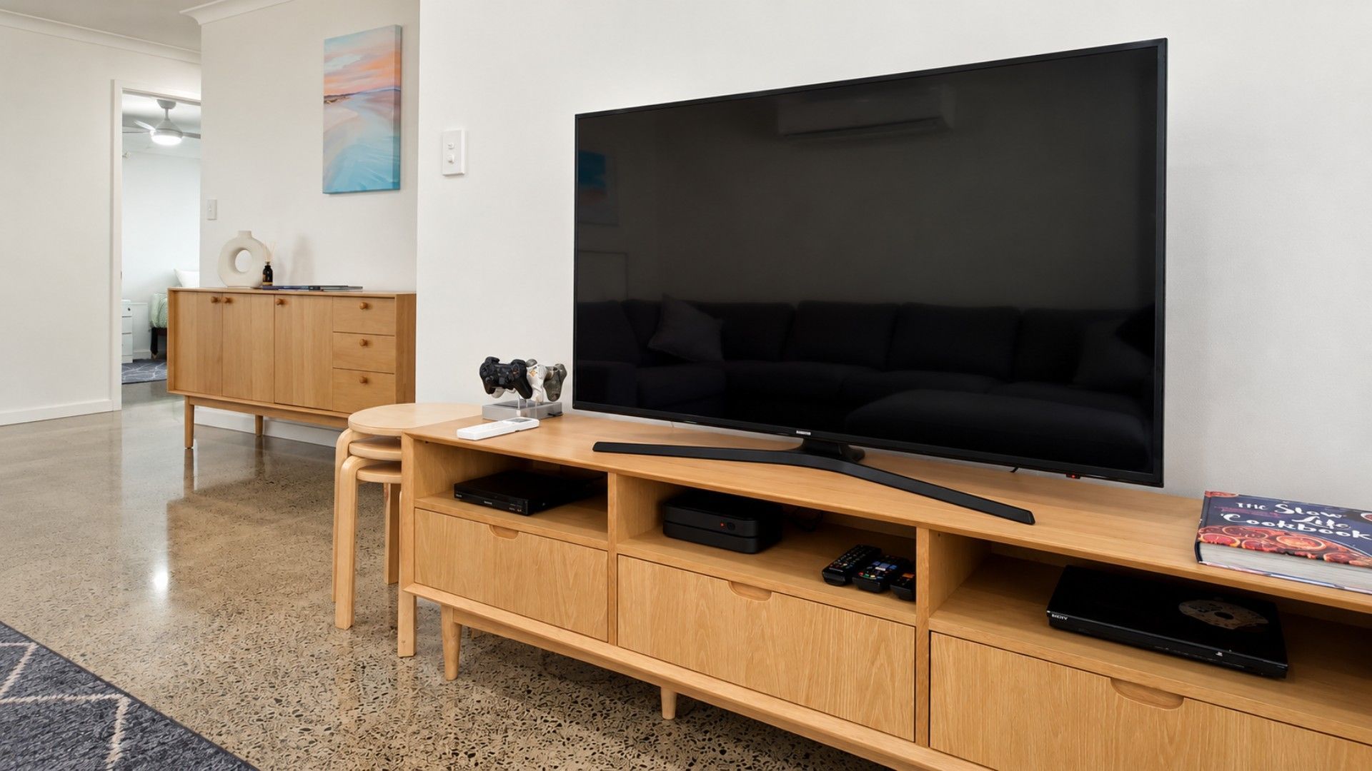 A modern living room with a large flat-screen TV, wooden entertainment unit, and a black sofa.