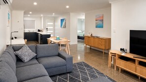 A modern living room with a grey sofa, a wooden TV stand, and a dining area.