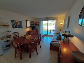 A dining area with a table and chairs, a sofa, a TV, and a balcony with a view. - Very nice 3-room apartment with indoor pool and golf course view in Cap d'Agde (LE CAP D AGDE)