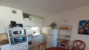 Eine kompakte Küche mit Waschmaschine, Mikrowelle und Kühlschrank. Ein Esstisch mit Stühlen und einer Vase steht bereit.
