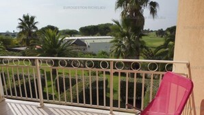 Ein Balkon mit einem rosafarbenen Stuhl, einem Metallgeländer und Blick auf einen Golfplatz sowie Gebäude.