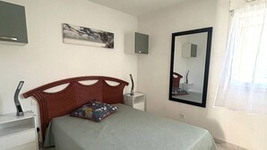Ein Schlafzimmer mit einem Bett, einem Nachttisch, einem wandmontierten Fernseher, einem Spiegel und einem Fenster mit Vorhängen.