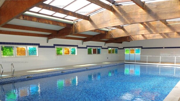 Ein Hallenbad mit Dachfenster, großen Glasfenstern und Fliesenboden.