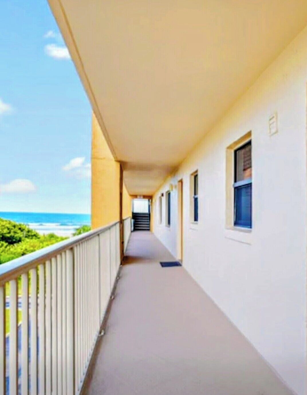 A corridor with a view of the ocean, a balcony with a railing, and a staircase leading to an upper level.