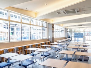 Ein Klassenzimmer mit Tischen, Stühlen, großen Fenstern und Schließfächern.