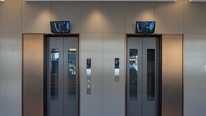 Un par de puertas de ascensor con pantallas digitales y una cámara de seguridad en la parte superior.