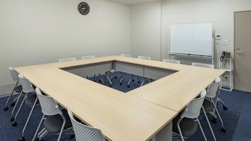 A conference room with a long table, chairs, a clock, a whiteboard, and a phone on a shelf.