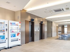 Ein moderner Aufzugsbereich mit Verkaufsautomaten, einem Konferenzraum und einem gefliesten Boden.