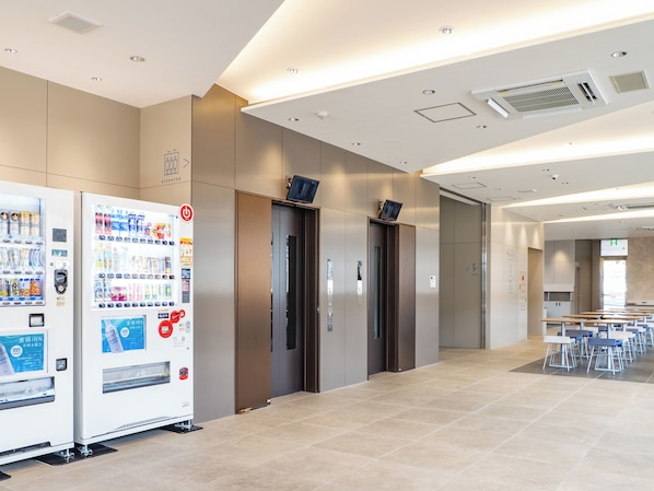 Un espace moderne avec ascenseurs, des distributeurs automatiques, une salle de conférence et un sol carrelé.