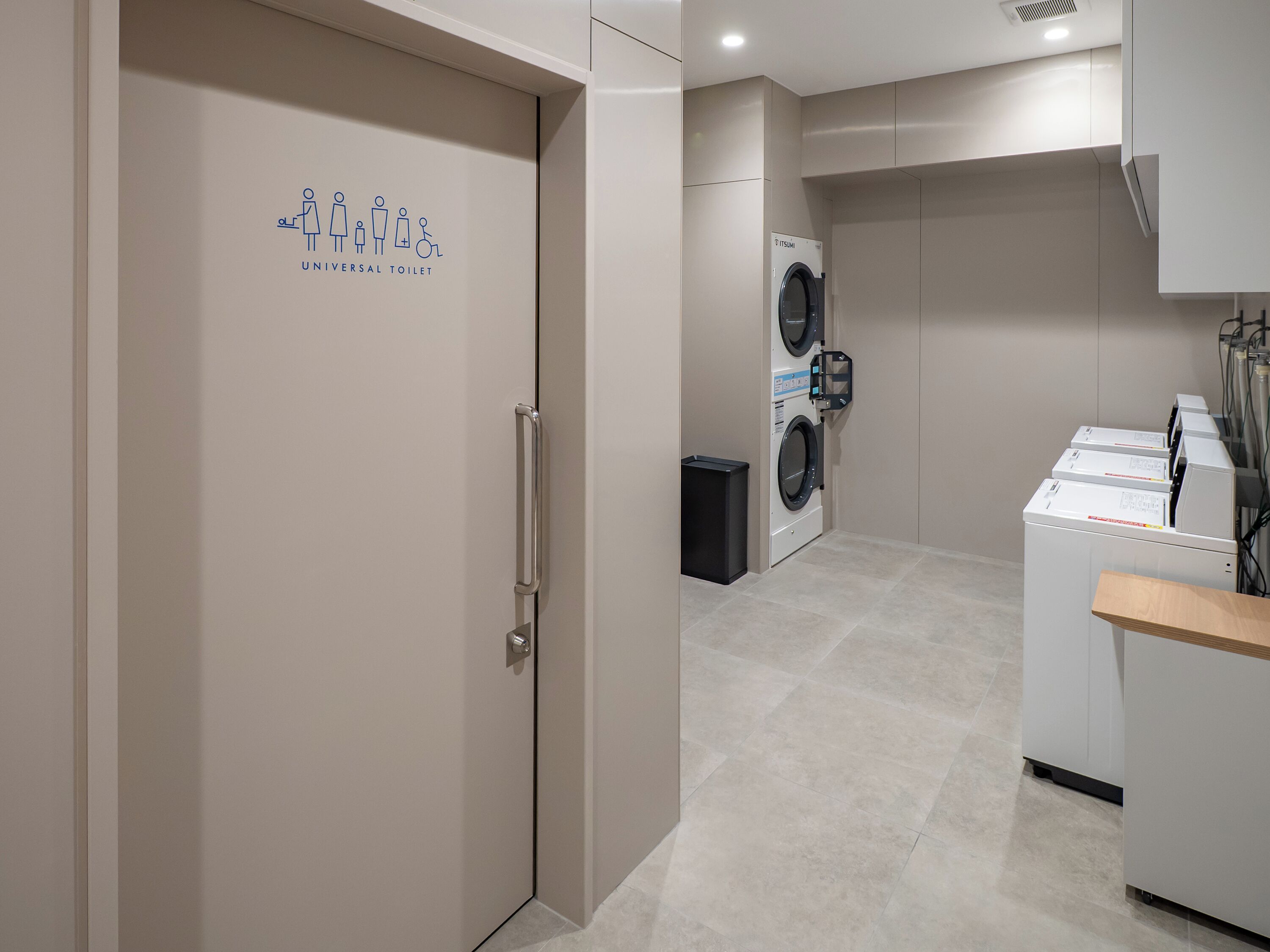 A modern laundry facility with a universal toilet sign, a washing machine, and a dryer.