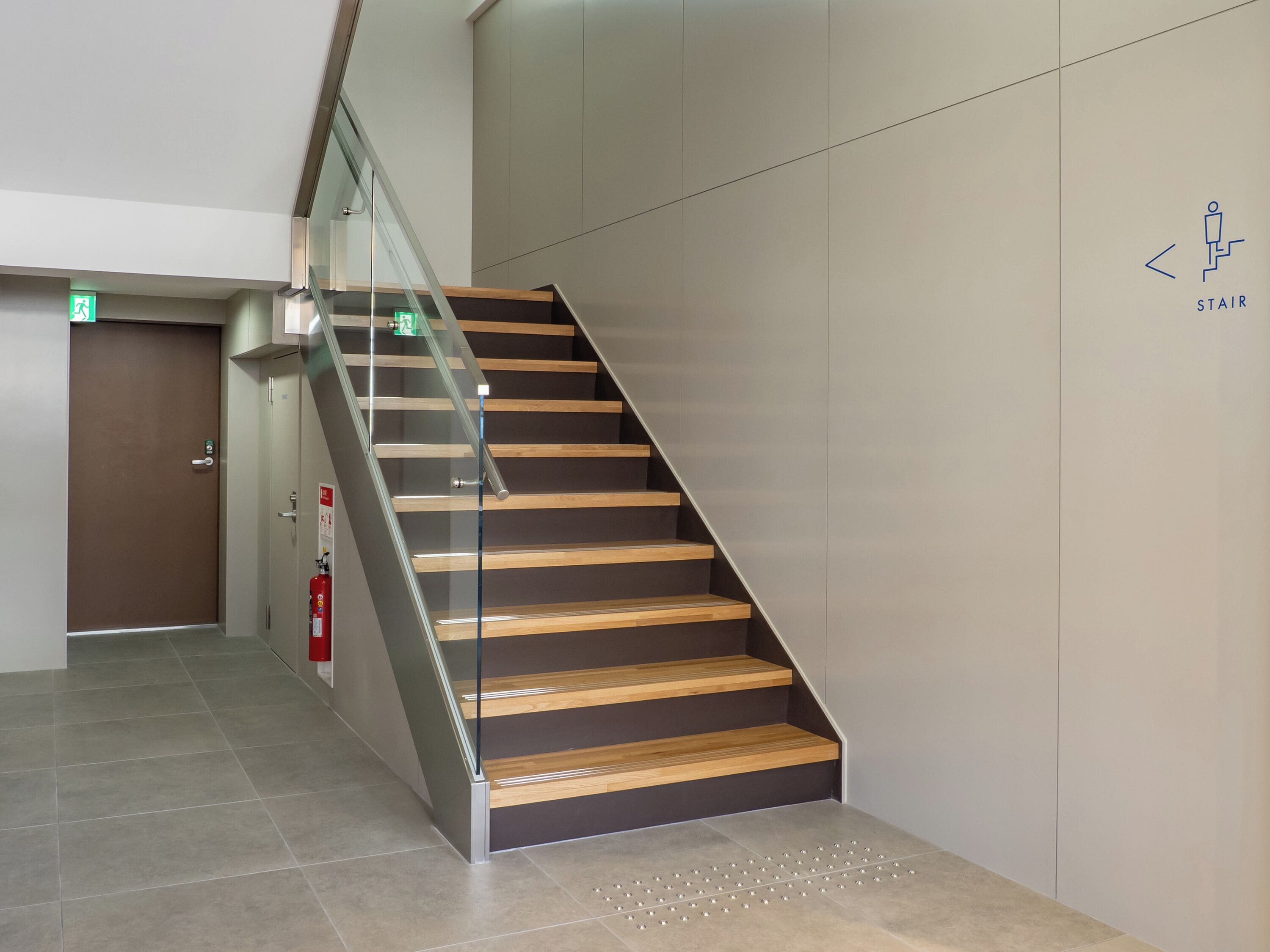 Una escalera moderna con barandillas de vidrio y peldaños de madera, que conduce a un ascensor.