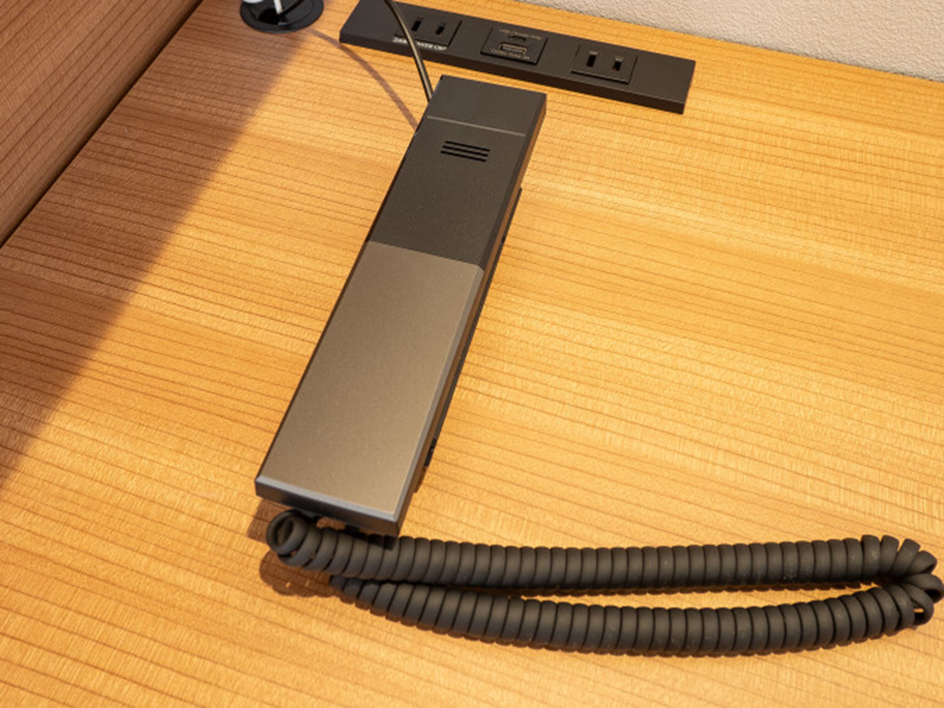 A black portable speaker with a coiled cord on a wooden surface.