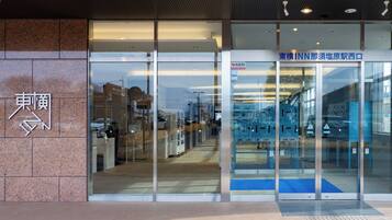 A building entrance with a glass door, a sign with Japanese characters, and a blue mat at the entrance.