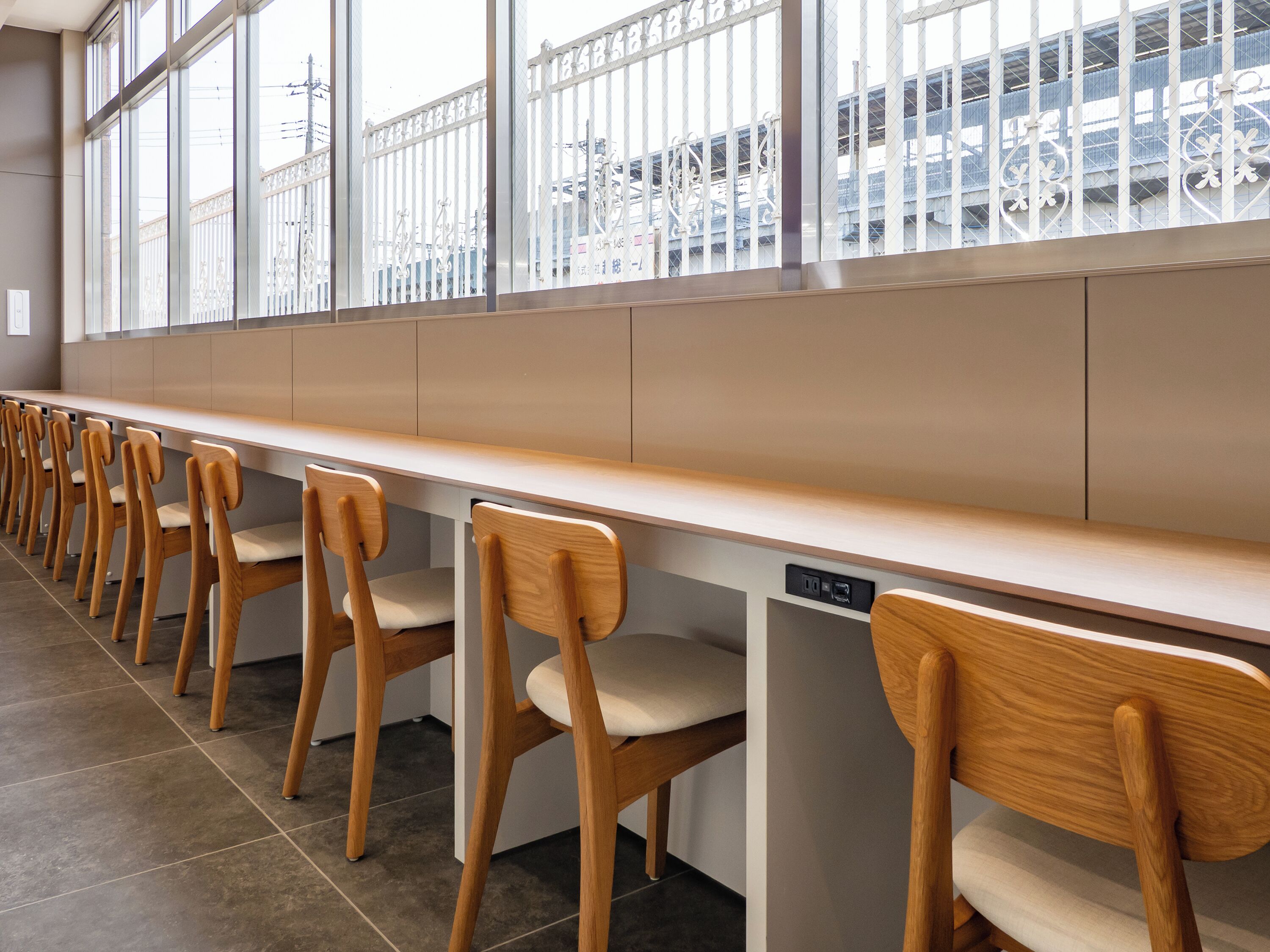 A row of wooden chairs with cushioned seats and backs, aligned along a long counter with a built-in dishwasher.
