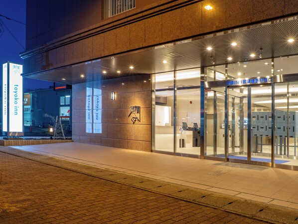 Entrada de un hotel con fachada de vidrio, una recepción visible y un cartel con el nombre del hotel.