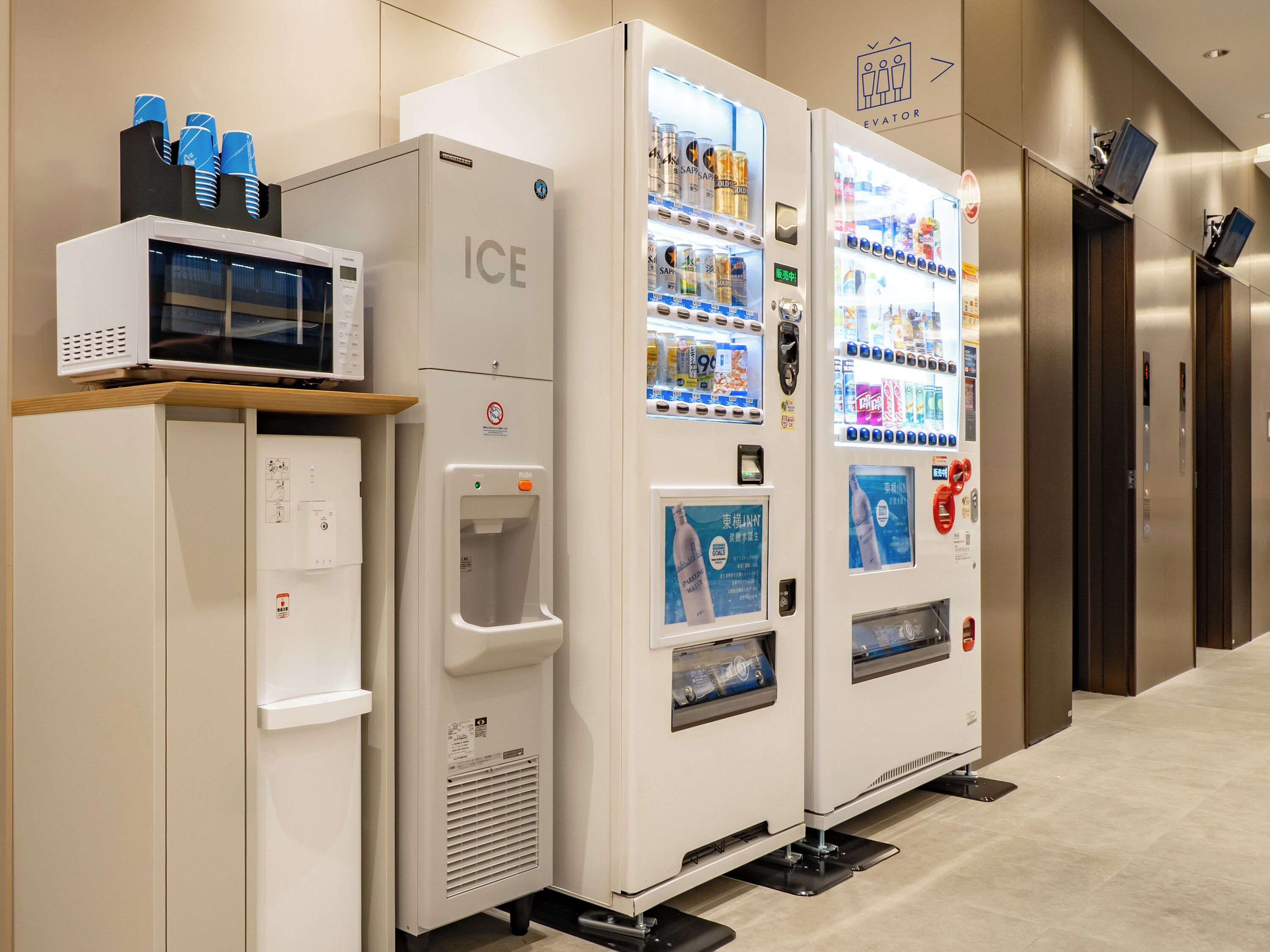 A vending machine labeled 'ICE' with a water dispenser and a microwave on top.