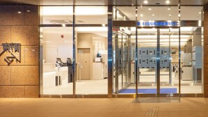 Entrada de un edificio con puertas de vidrio, un felpudo azul y un letrero con caracteres japoneses.