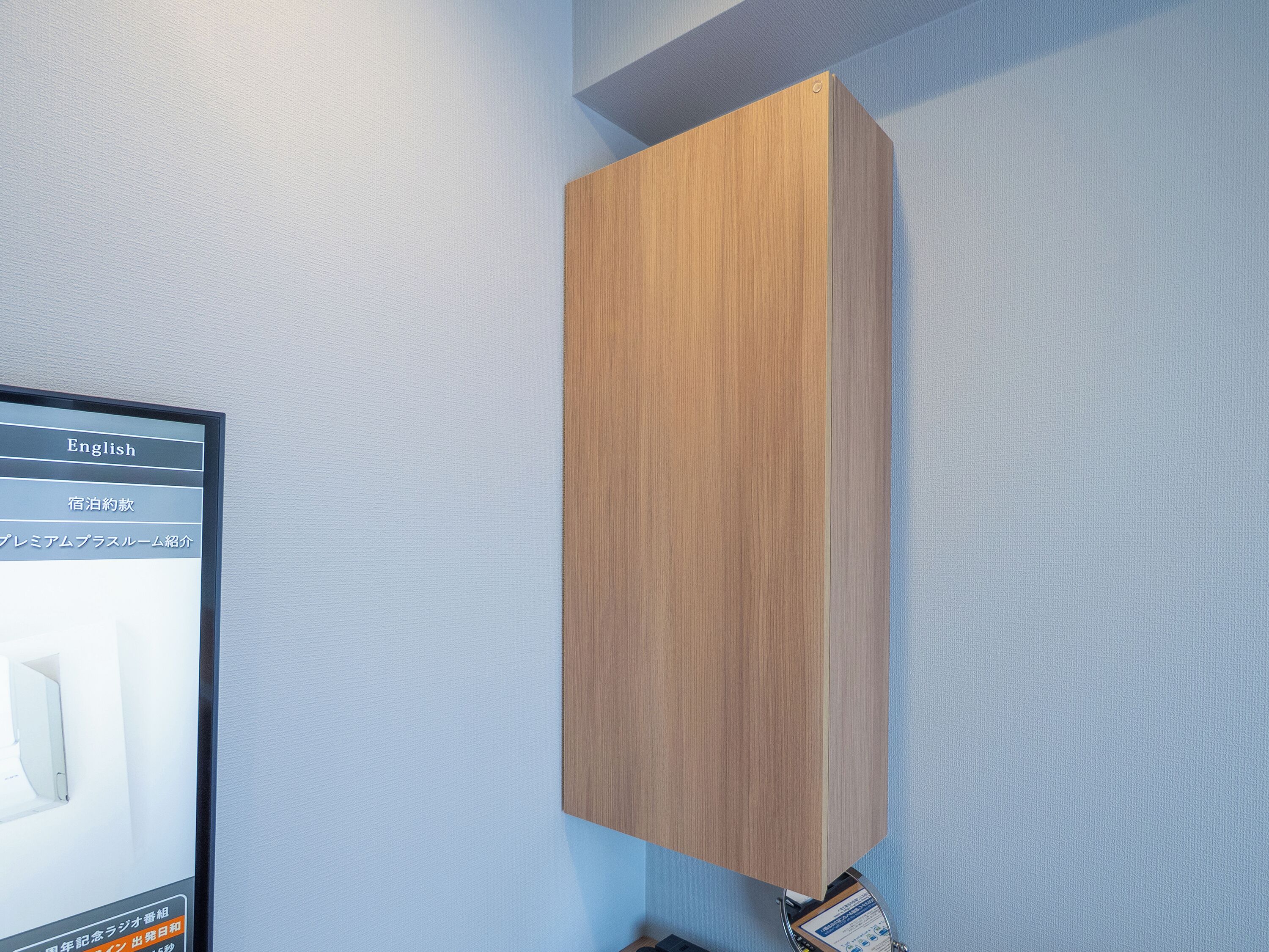 A wooden cabinet against a textured wall, with a monitor displaying text in English and Japanese.