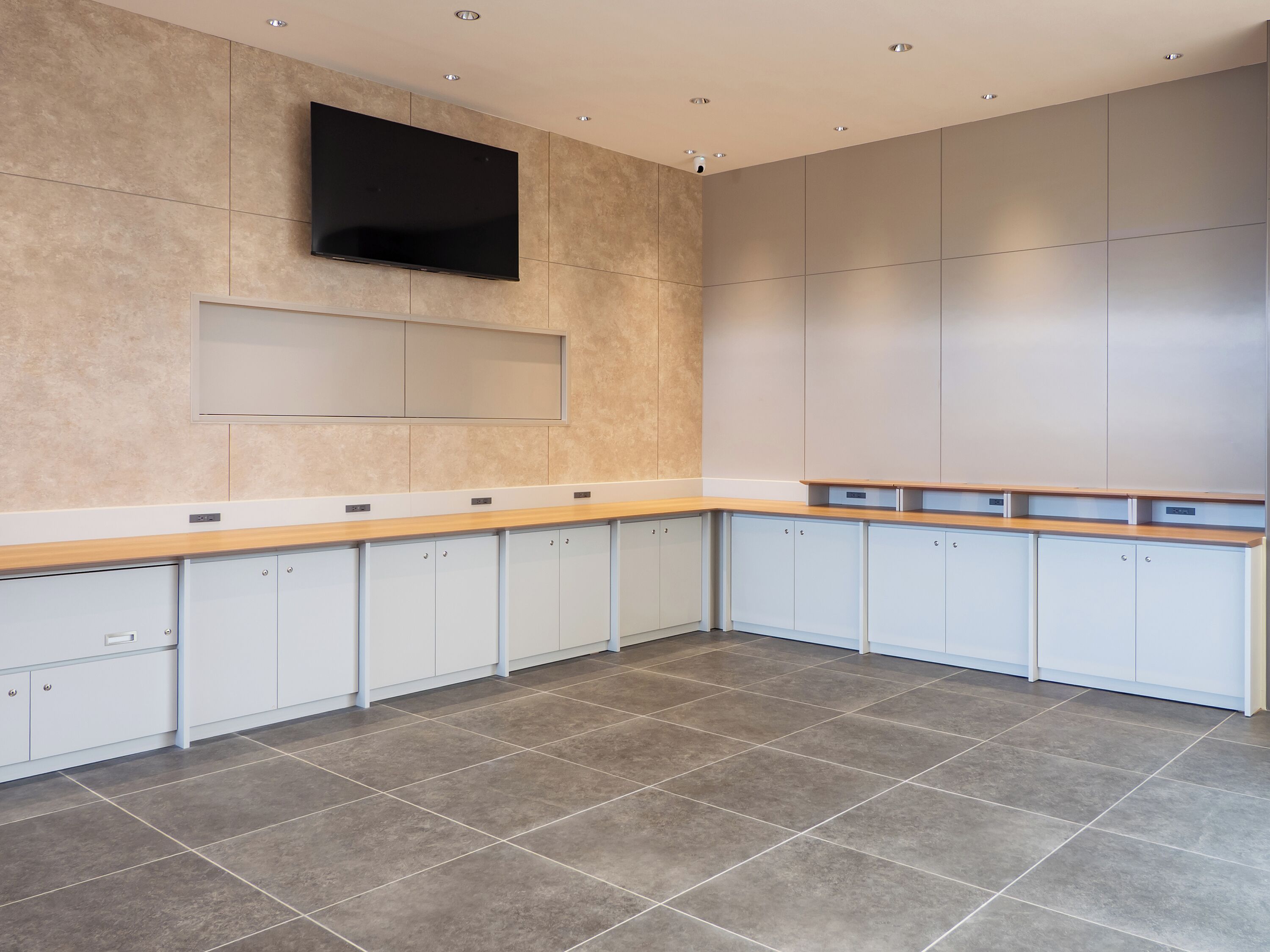 A modern kitchen with a large flat-screen TV, light-colored cabinets, and a wooden countertop.