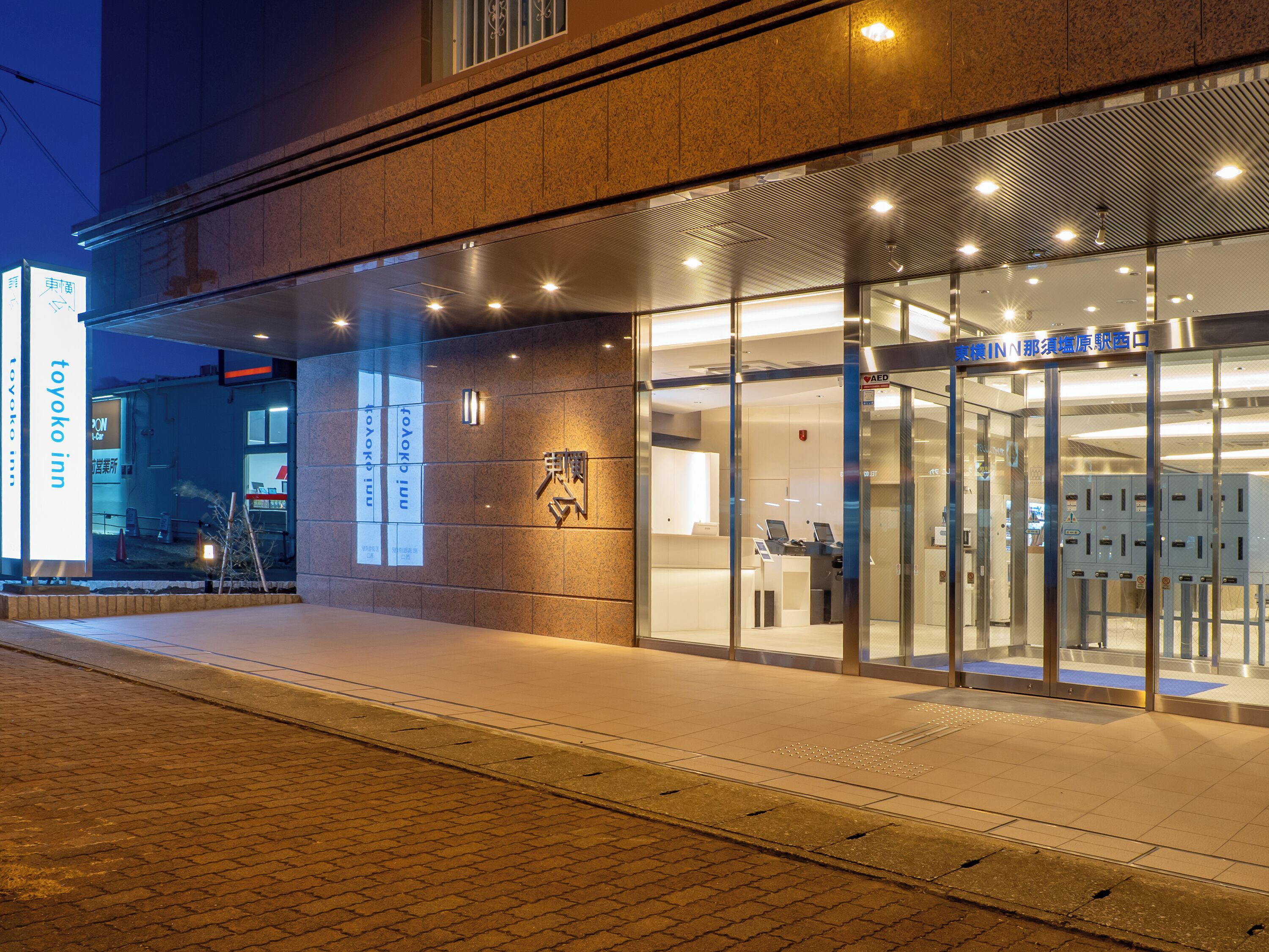 A hotel entrance with a glass facade, a reception desk, and a sign indicating 'TOYOKO INN'.