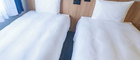 A hotel room with two single beds, a wooden headboard, a control panel, and a blue curtain.