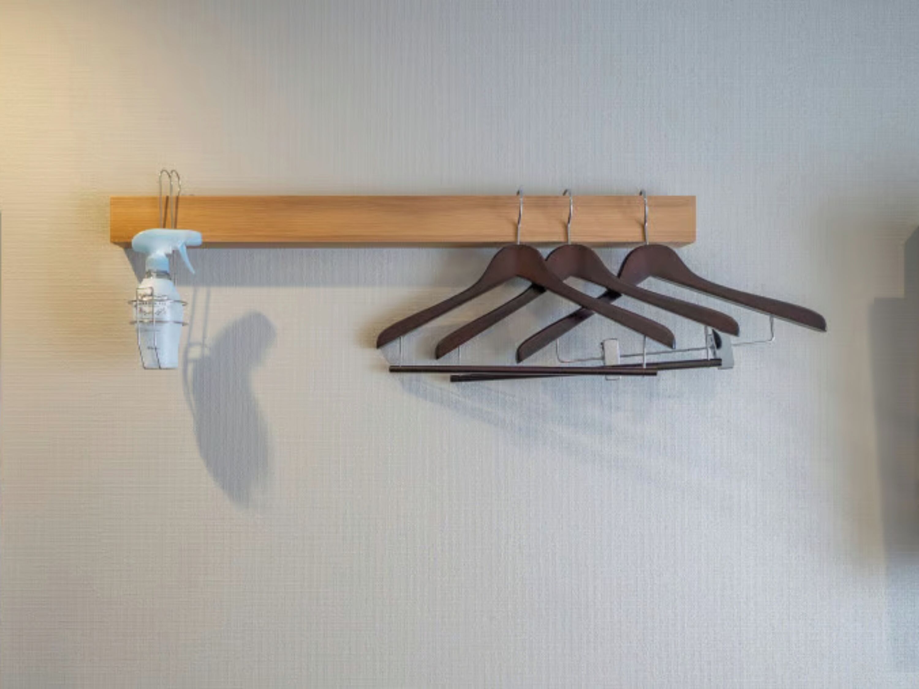 A wall-mounted wooden rack with three brown hangers and a white spray bottle.
