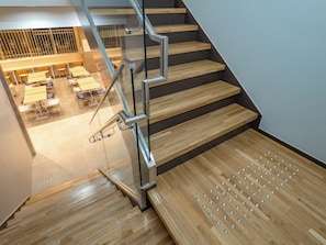 Un escalier avec des marches en bois et des rampes en métal, menant à un espace repas équipé de tables et de chaises.