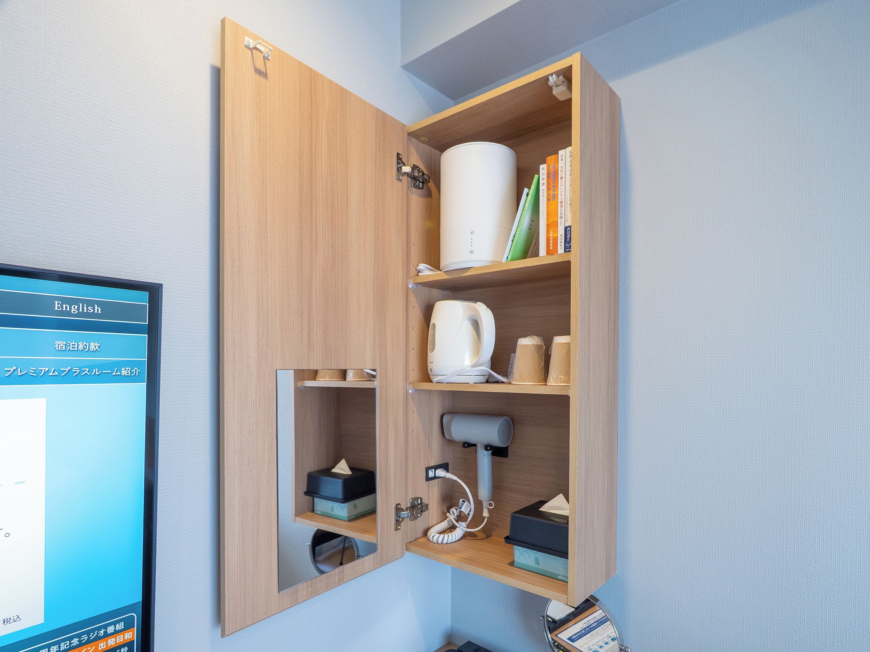 A wooden cabinet with shelves containing books, a kettle, a coffee maker, and a telephone.