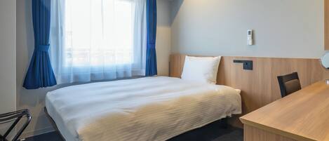 Habitación de hotel con cama, escritorio, silla y ventana con cortinas.