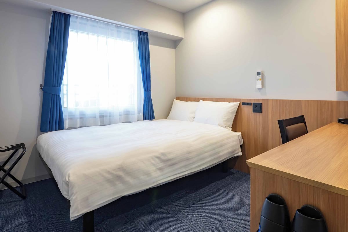 A hotel room with a bed, a desk, a chair, and a window with curtains.