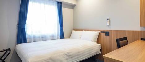 Una habitación de hotel con cama, escritorio, silla y ventana con cortinas.