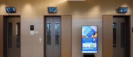 A modern lobby with three elevators, a digital advertisement board, and a clean tiled floor.