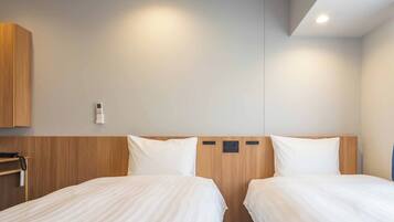 A hotel room with two beds, a wooden headboard, a wall-mounted thermostat, and a small shelf with a bottle.