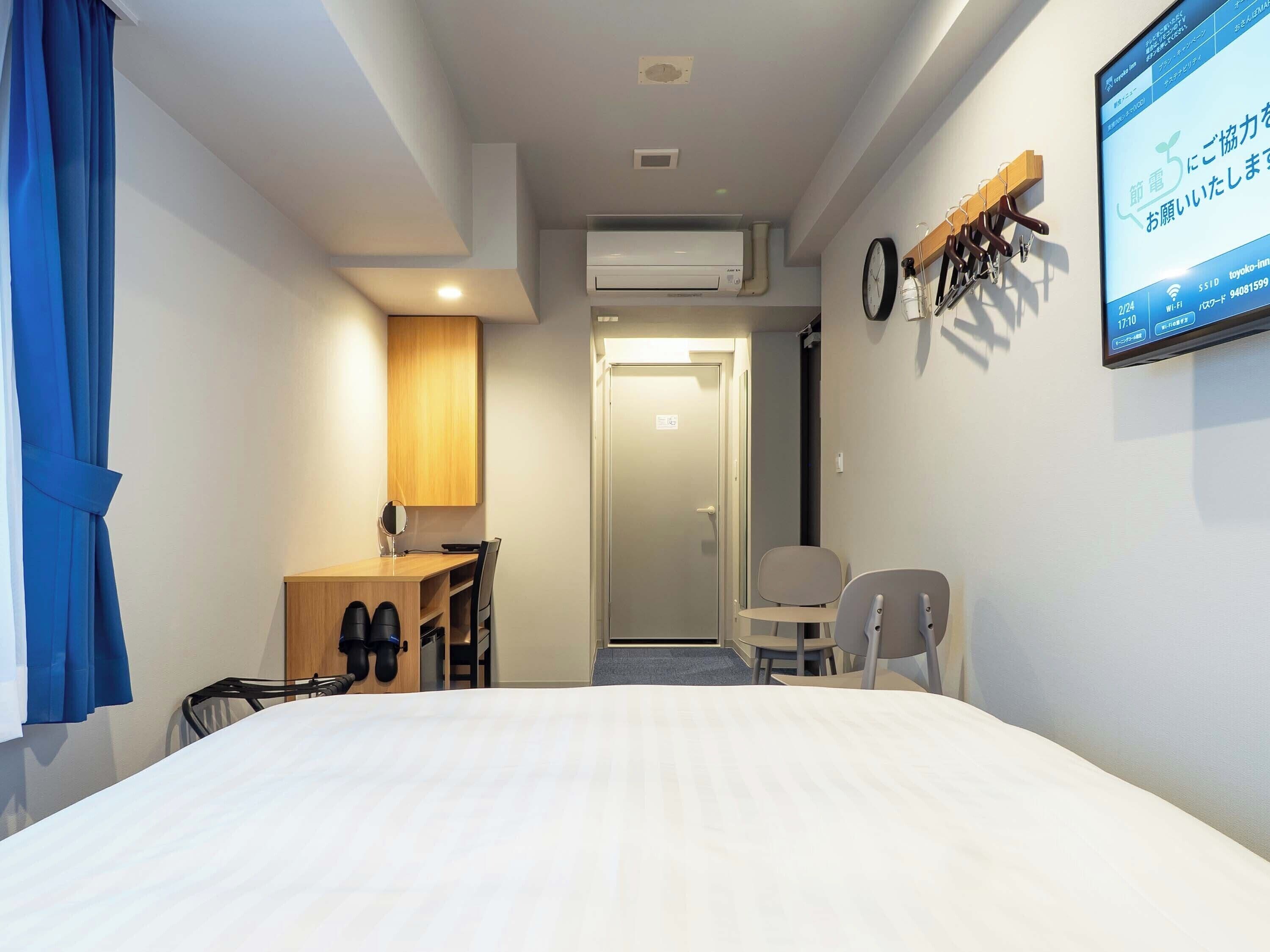 A hotel room with a bed, a desk, a chair, a TV, and an air conditioning unit.