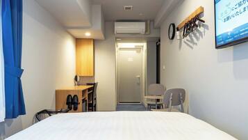 A hotel room with a bed, a desk, a chair, a TV, and an air conditioning unit.