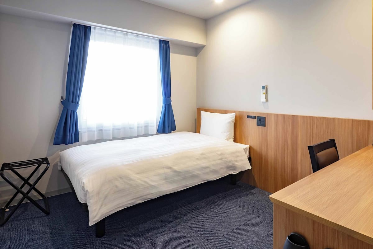 A hotel room with a bed, a desk, and a chair.