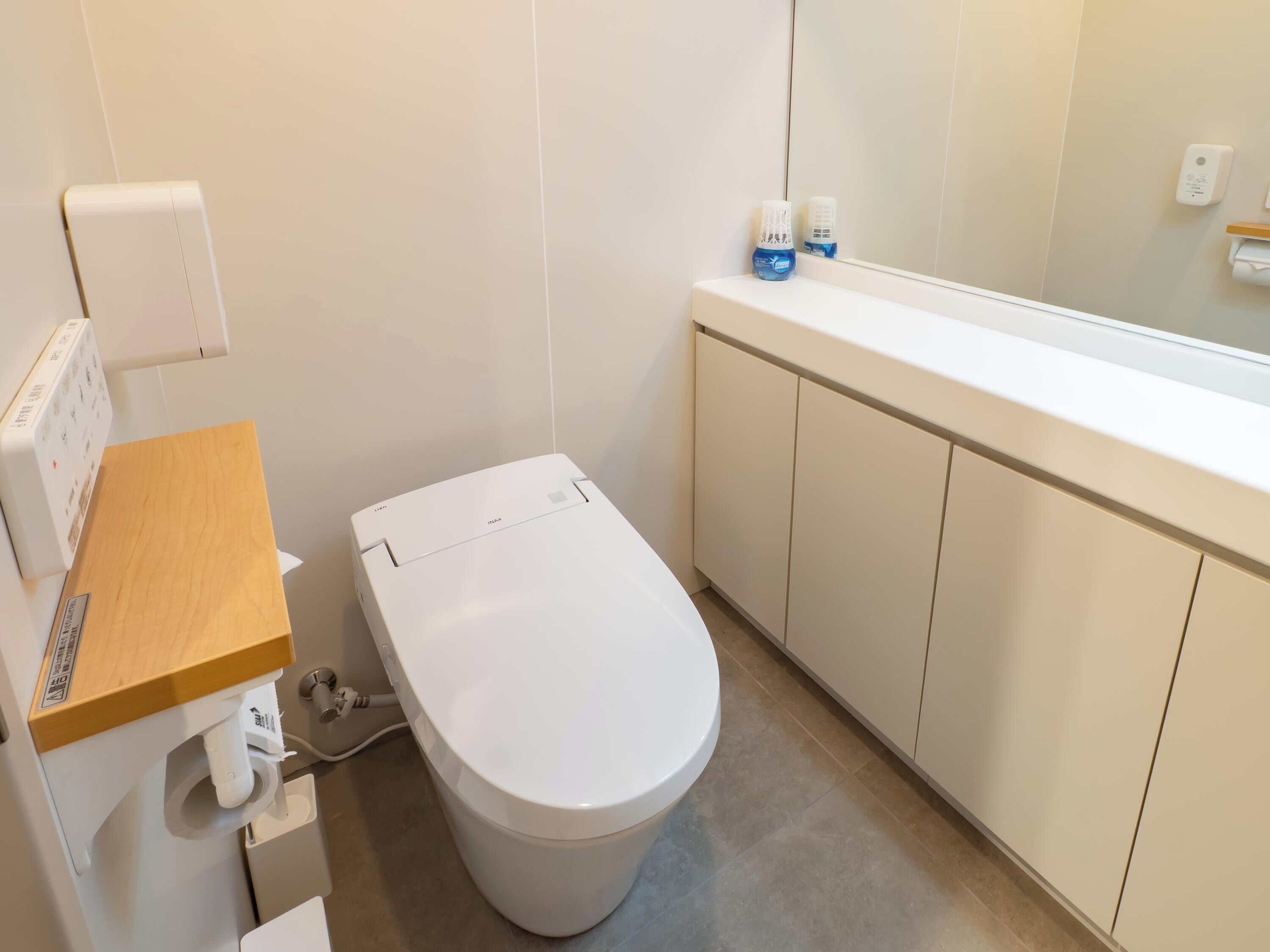 Un baño moderno con inodoro, tocador de madera, espejo y un armario blanco.