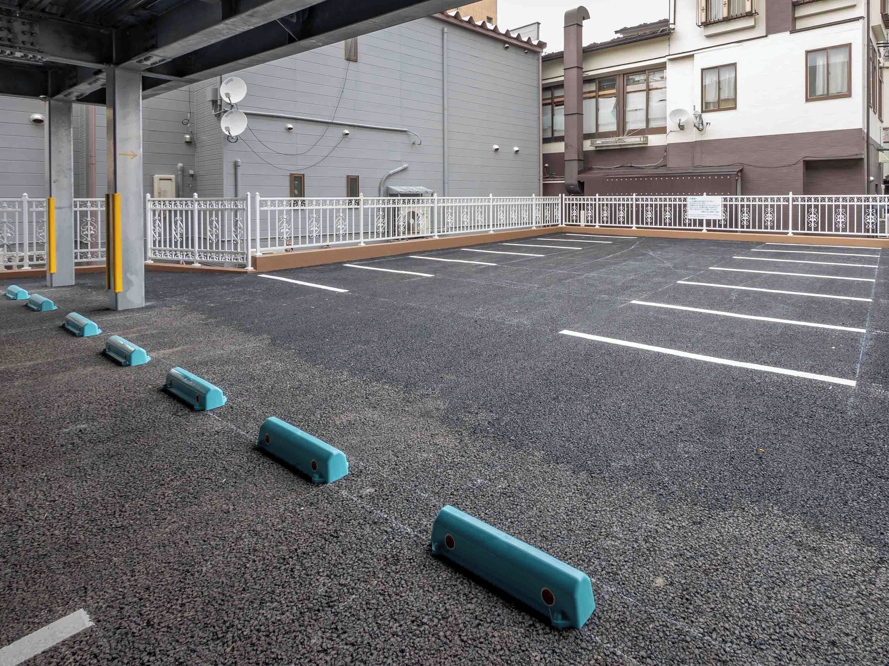 A parking lot with marked spaces and bollards, a building with a grey facade, and a white fence.