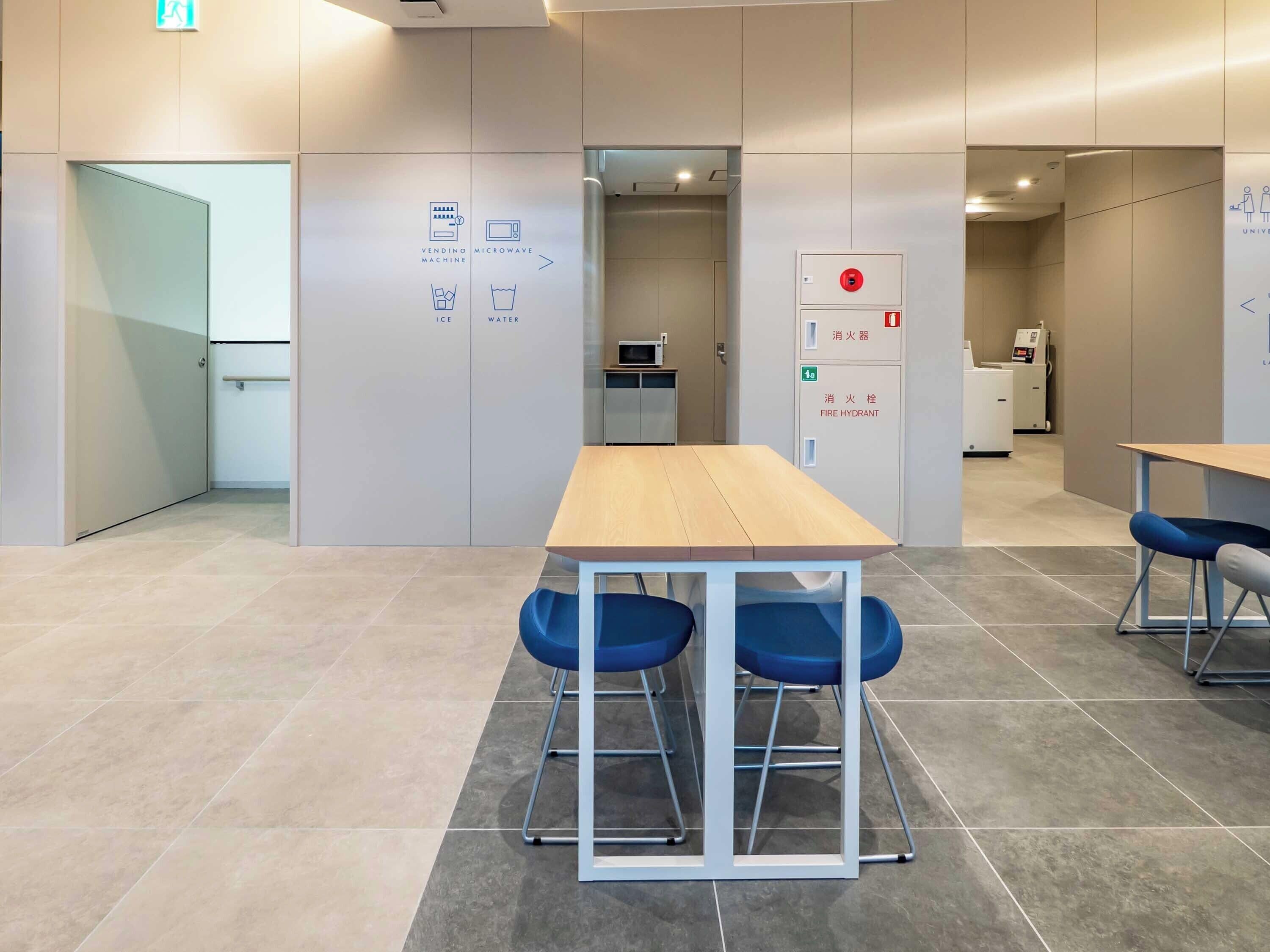 A modern meeting room with a wooden table and blue chairs, a vending machine, and a microwave.
