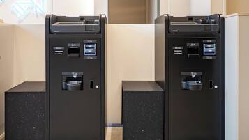 Two self-service kiosks with card readers, a small trash bin, and a neon sign on the wall.