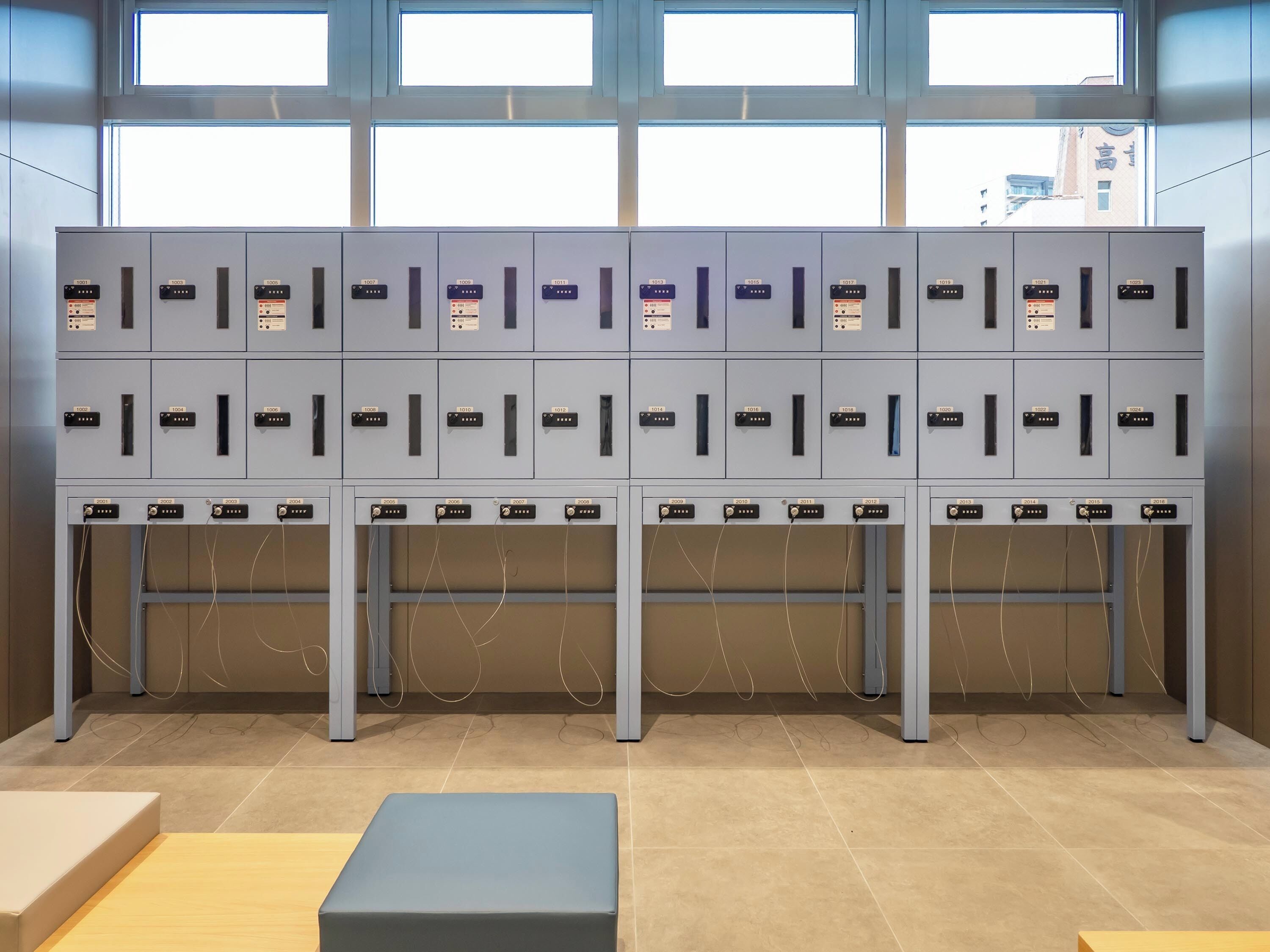 A row of grey lockers with numbered labels, a tiled floor, and a bench in the foreground.
