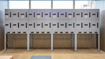 A row of grey lockers with numbered labels, a tiled floor, and a bench in the foreground.