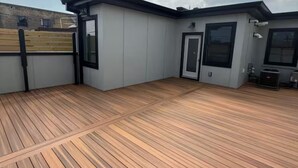 A rooftop deck with a wooden floor, a small building with a door and windows, and a cloudy sky in the background.